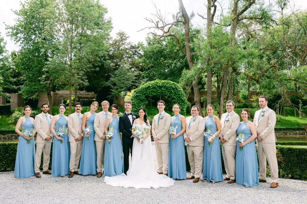 Photo de groupe des mariés et du cortège en extérieur, tenues beige et bleu